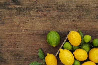 Many fresh lemons and limes with leaves on wooden table, flat lay. Space for text