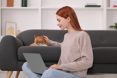 Woman stroking cat while working with laptop at home