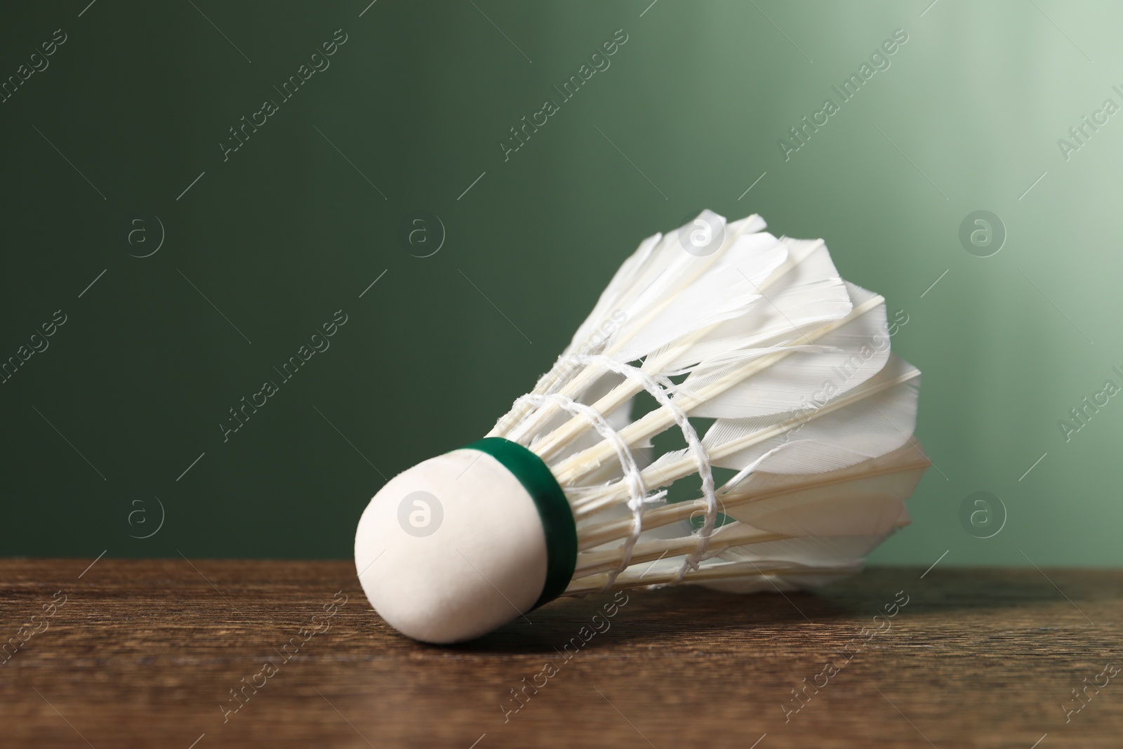 Photo of Feather badminton shuttlecock on wooden table against green background, closeup