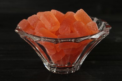 Photo of Tasty orange jelly candies in glass bowl on black table, closeup