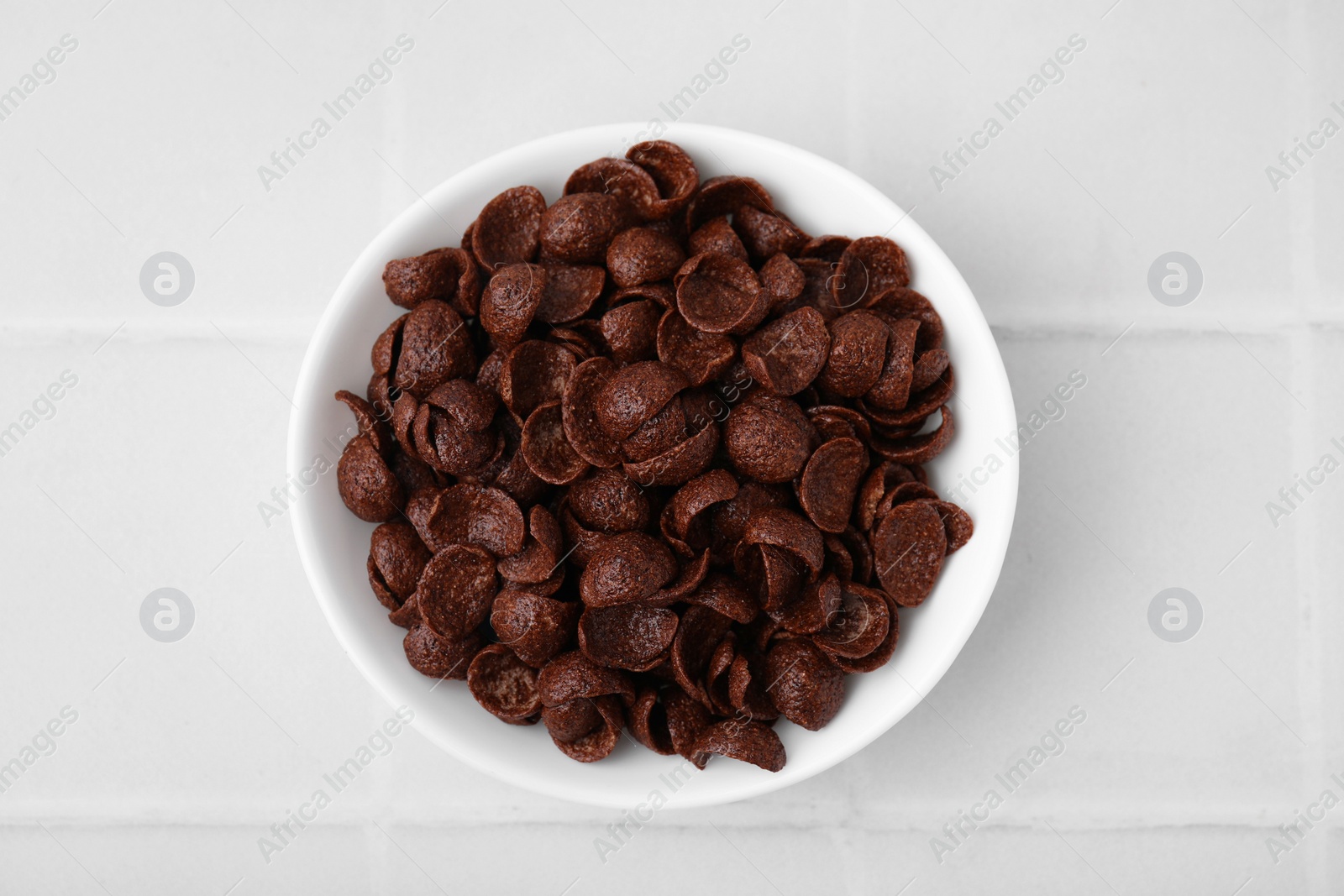 Photo of Breakfast cereal. Chocolate corn flakes in bowl on white tiled table, top view