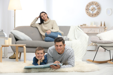 Photo of Father and his son reading book while mother resting on sofa at home. Winter vacation