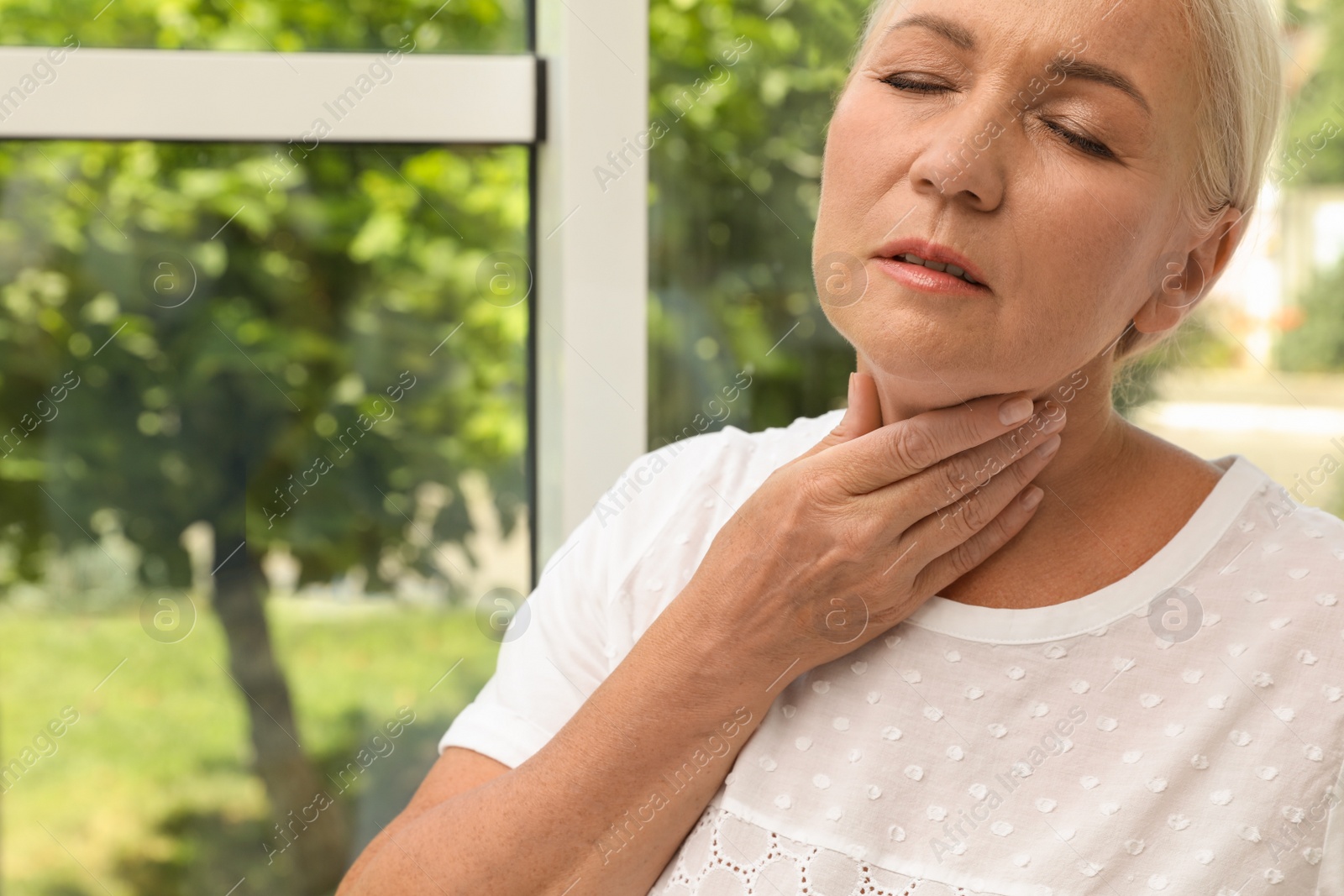 Photo of Mature woman doing thyroid self examination near window, closeup. Space for text