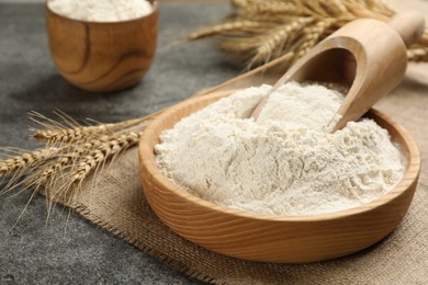 Photo of Plate with wheat flour and wooden scoop on grey table