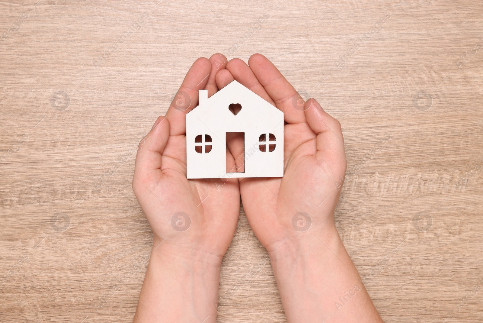 Photo of Home security concept. Man holding house model at wooden table, top view