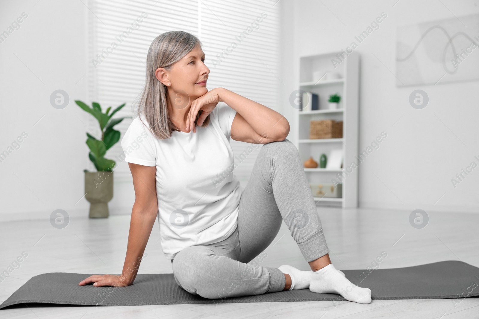 Photo of Senior woman sitting on mat at home. Yoga practice