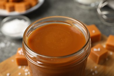 Photo of Yummy salted caramel in glass jar on table, closeup