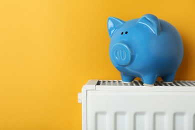 Photo of Piggy bank on heating radiator against orange background, space for text