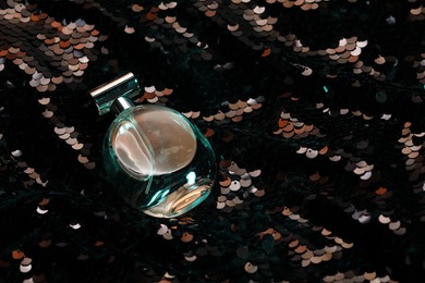 Photo of Luxury perfume in bottle on fabric with shiny sequins, above view
