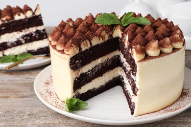Delicious tiramisu cake with mint leaves on wooden table, closeup