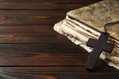 Photo of Wooden Christian cross and old Bible on table, closeup. Space for text