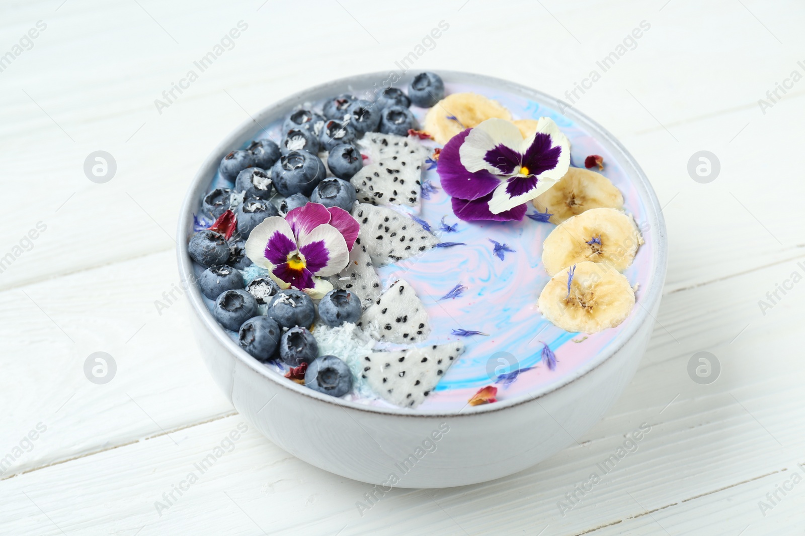 Photo of Delicious smoothie bowl with fresh fruits, blueberries and flowers on white wooden table, closeup