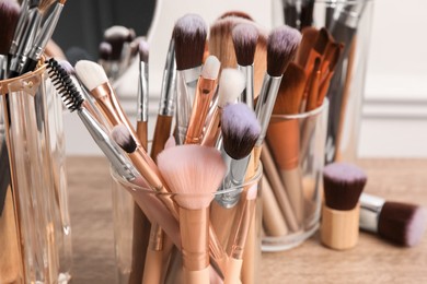 Photo of Set of professional makeup brushes and mirror on wooden table, closeup