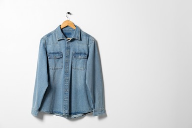 Hanger with denim shirt on white wall, space for text