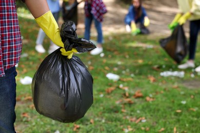 Photo of Man holding plastic bag with garbage in park, closeup. Space for text