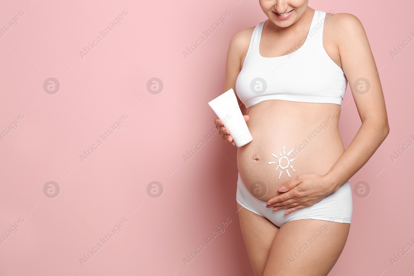 Photo of Sun painted with body cream on pregnant woman's belly against color background, closeup. Space for text