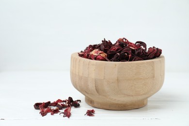 Photo of Hibiscus tea. Bowl with dried roselle calyces on white wooden table, closeup. Space for text