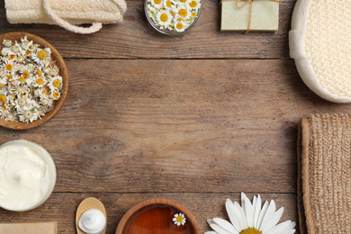 Frame of chamomile flowers and cosmetic products on wooden table, space for text