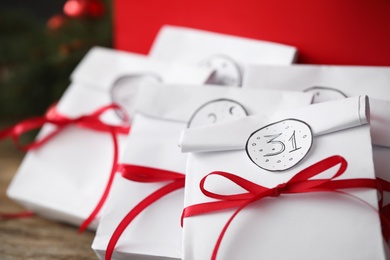 Small paper bags with red ribbons on table, closeup. New Year advent calendar