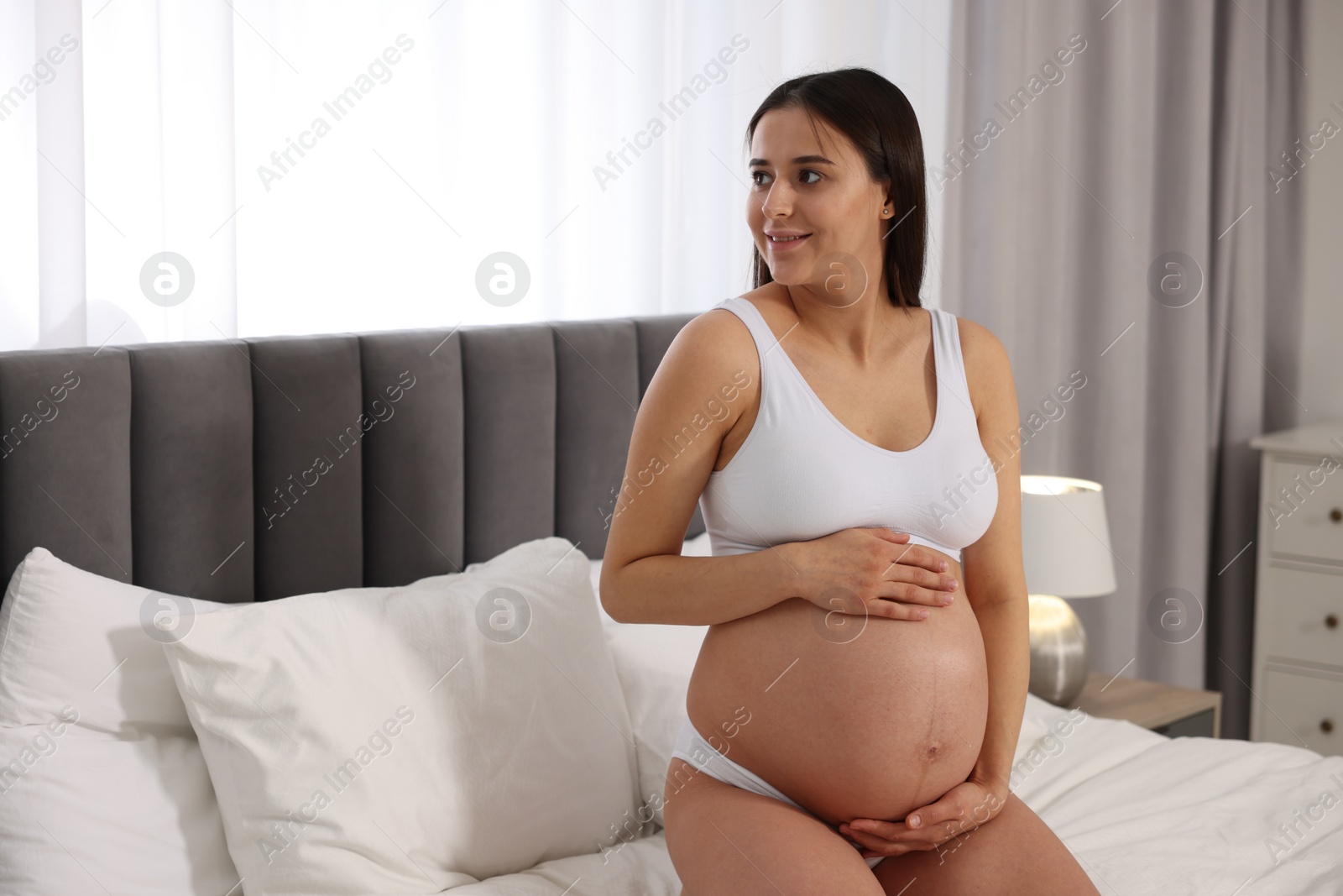 Photo of Beautiful pregnant woman in stylish comfortable underwear on bed at home, space for text