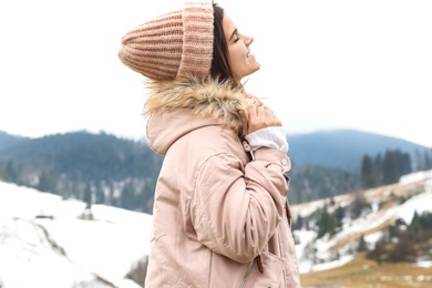 Young woman in warm clothes near snowy hill. Winter vacation