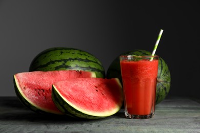 Photo of Delicious watermelons and glass of smoothie on light blue wooden table against dark grey background