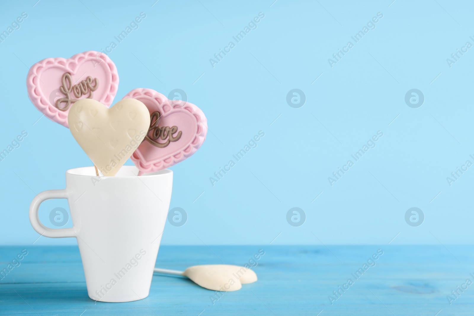 Photo of Heart shaped lollipops made of chocolate on light blue background, space for text