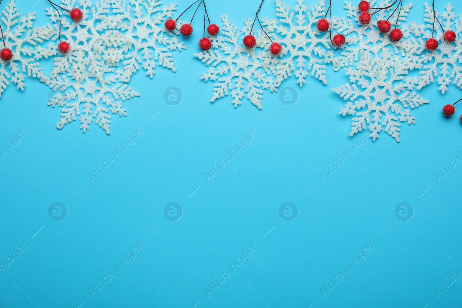 Photo of Beautiful decorative snowflakes and red berries on light blue background, flat lay. Space for text