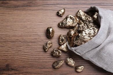 Overturned sack of gold nuggets on wooden table, flat lay. Space for text