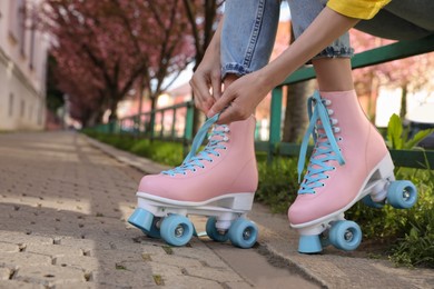 Photo of Young woman putting on roller skates outdoors, closeup