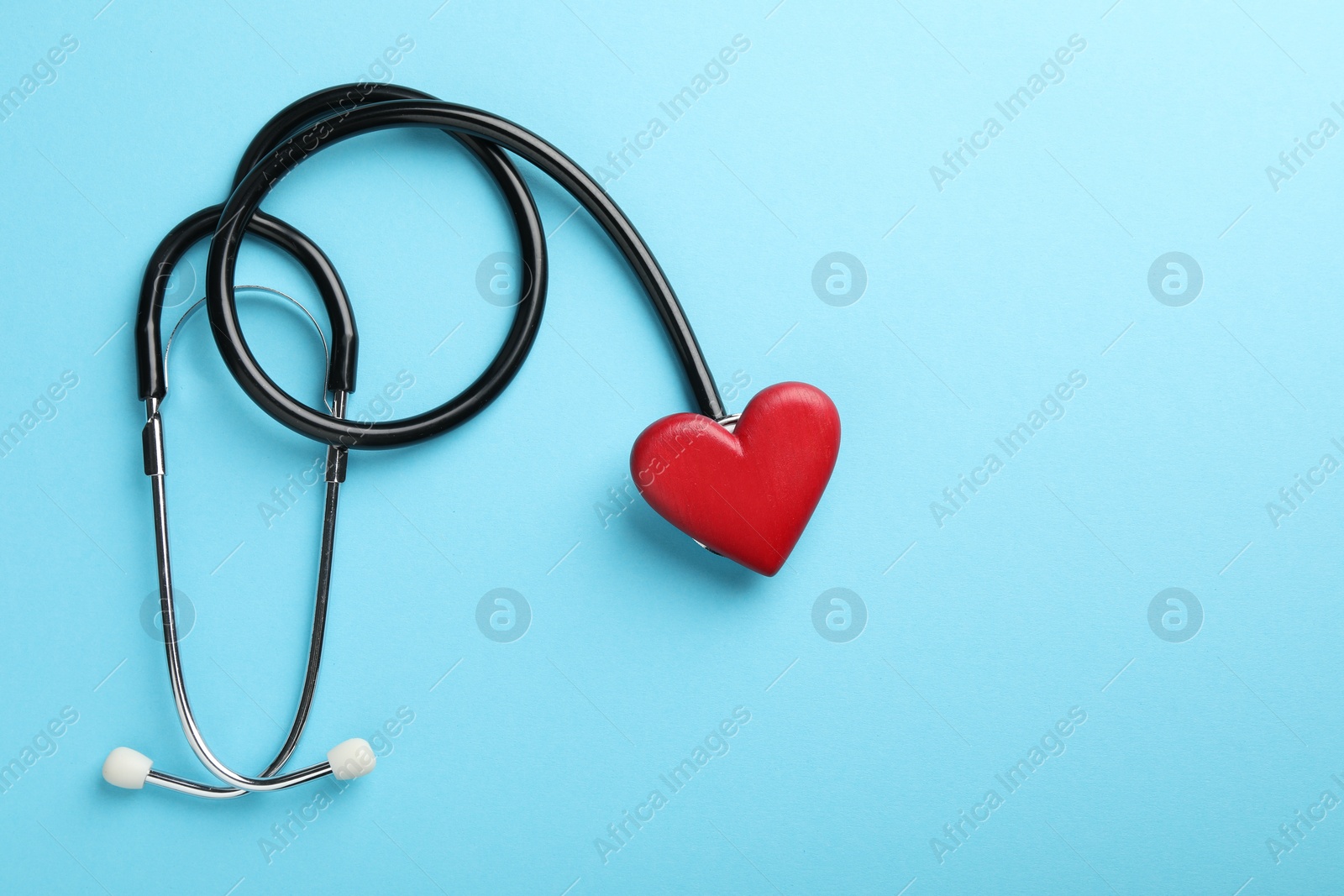 Photo of Stethoscope and red heart on light blue background, top view. Space for text