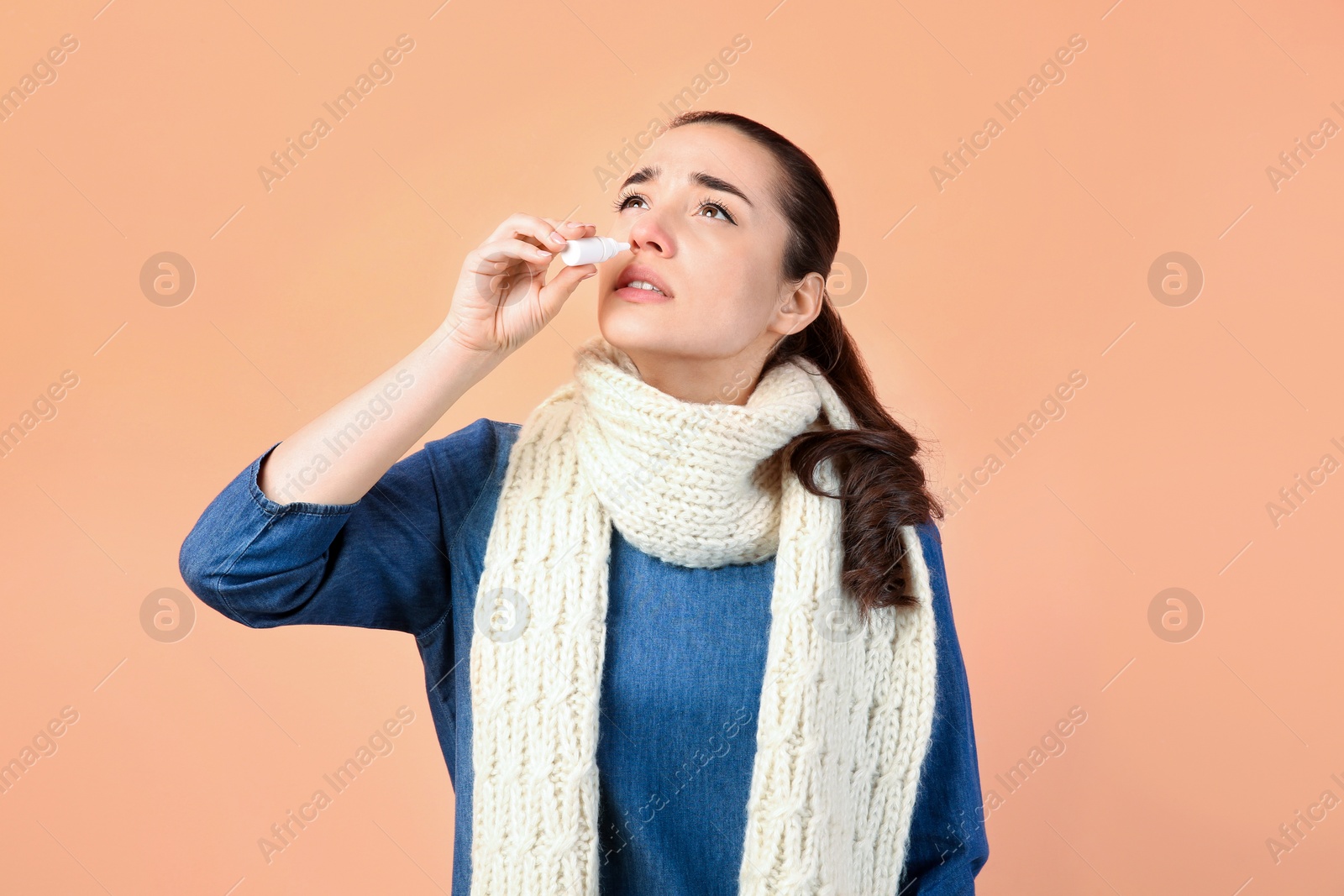 Photo of Woman using nasal spray on peach background