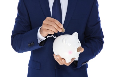 Photo of Young businessman putting money into piggy bank on white background, closeup