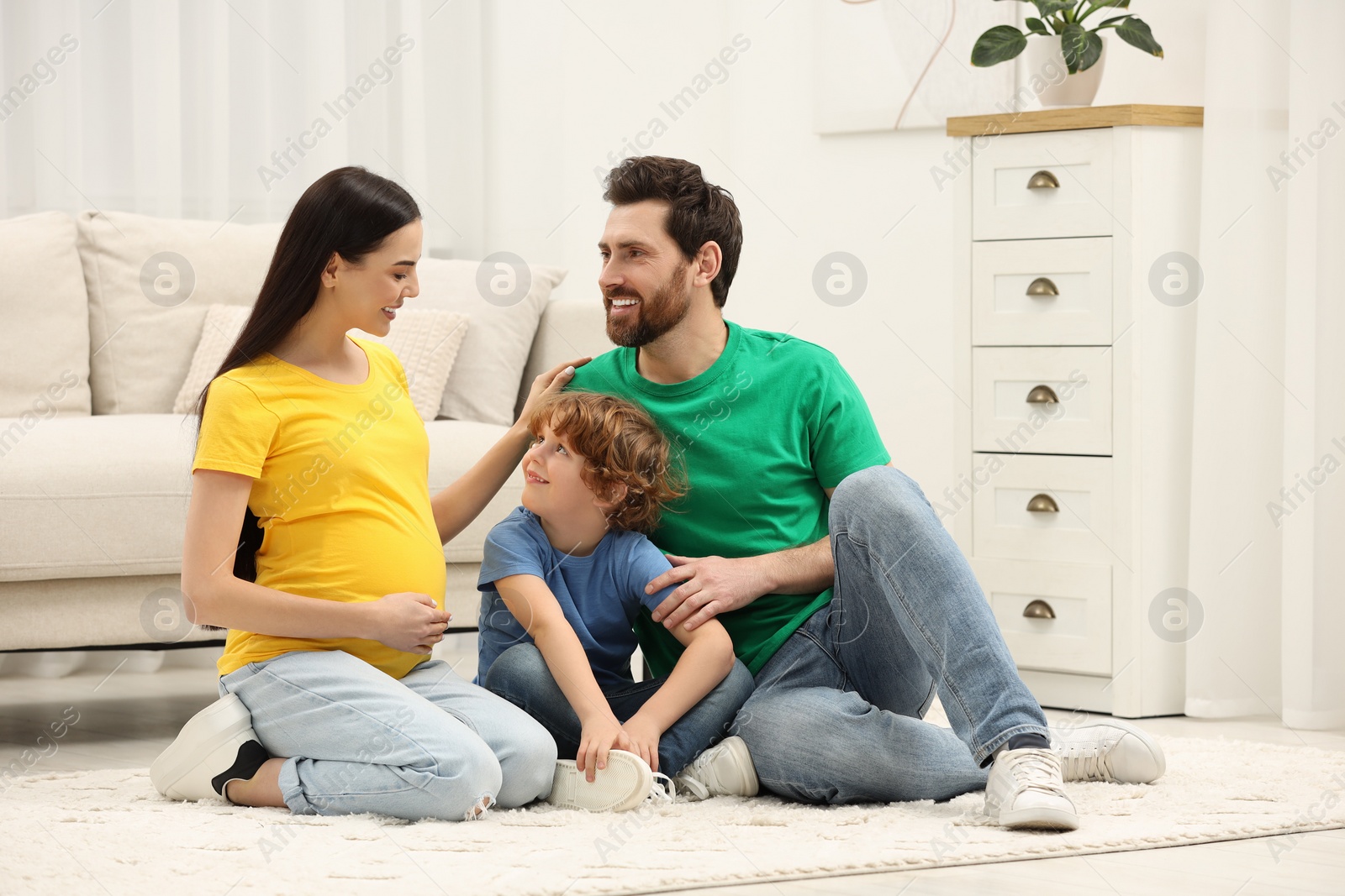 Photo of Family portrait of pregnant mother, father and son sitting on floor in house