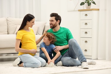 Family portrait of pregnant mother, father and son sitting on floor in house
