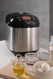 Breadmaker and different products on white wooden table indoors