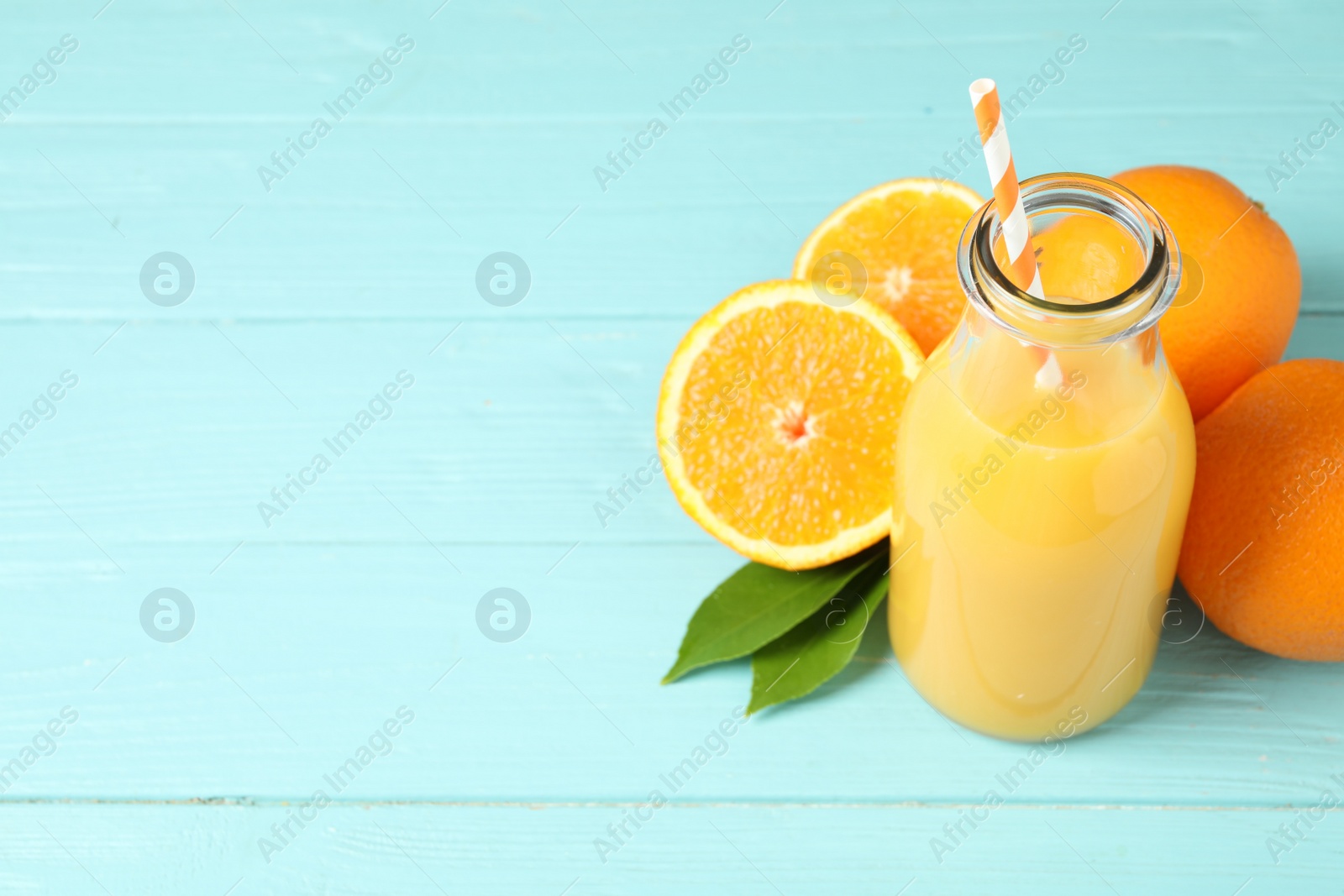 Photo of Bottle of orange juice and fresh fruits on light blue wooden table. Space for text