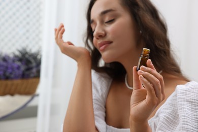 Beautiful young woman with bottle of essential oil indoors, selective focus