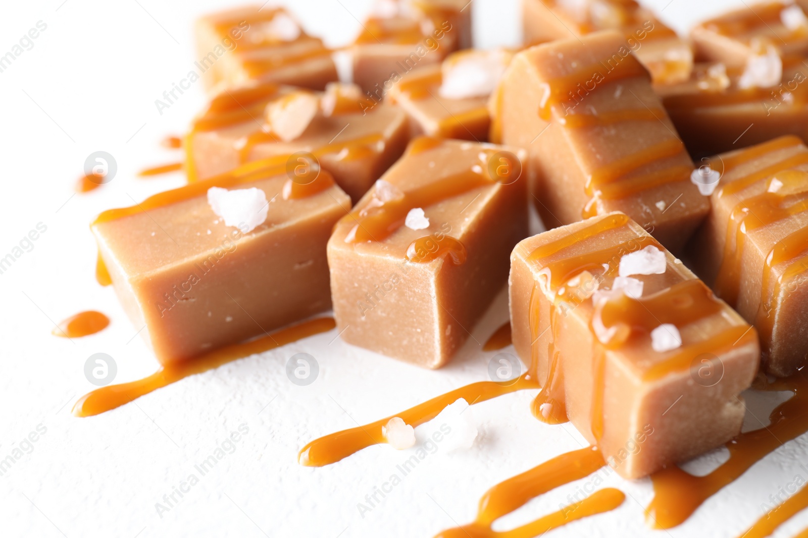 Photo of Tasty candies, caramel sauce and salt on white table, closeup