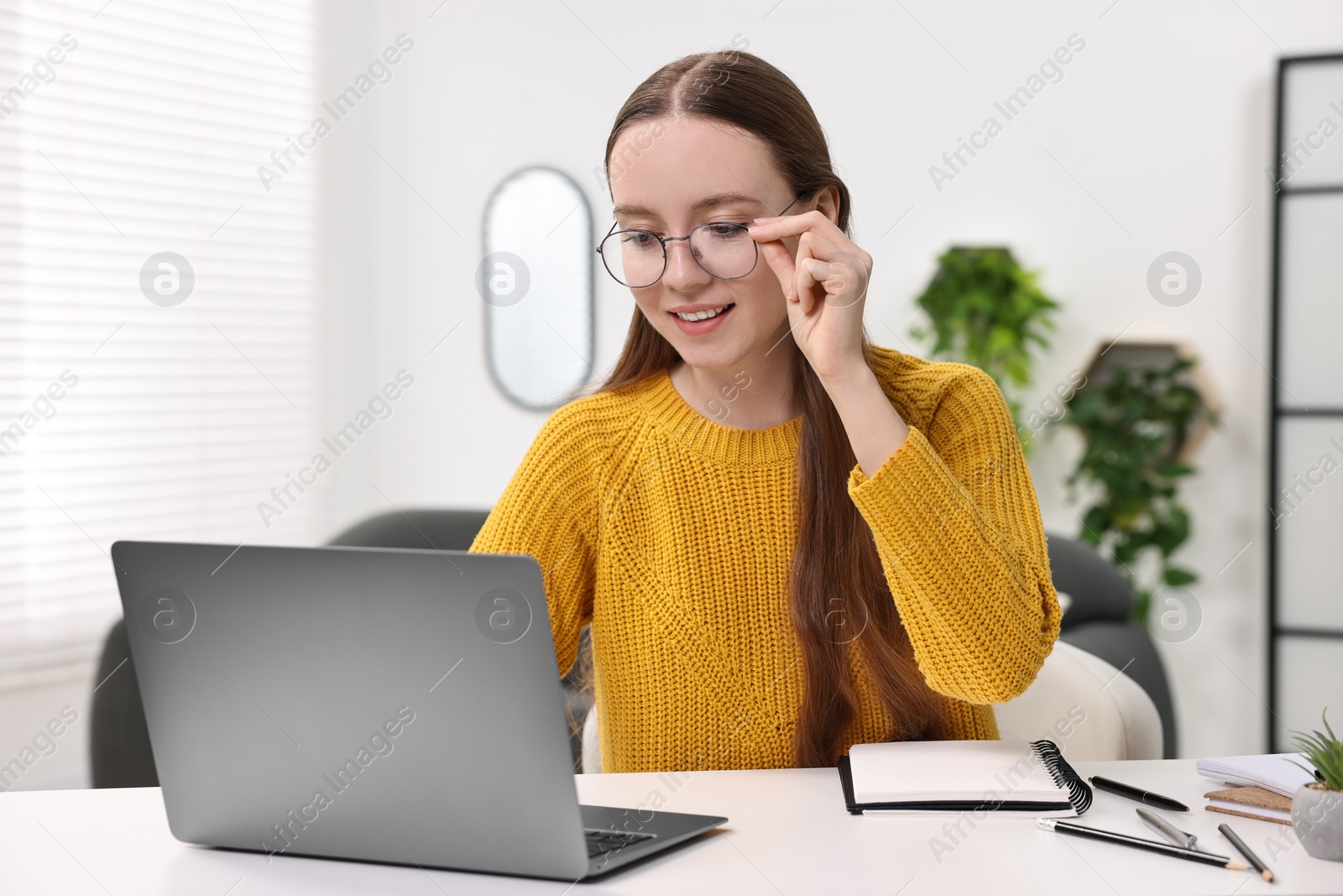 Photo of E-learning. Young woman using laptop during online lesson at white table indoors