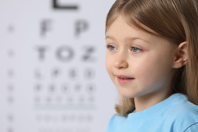 Photo of Cute little girl against vision test chart, closeup