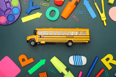 Photo of Yellow school bus and stationery on green background, flat lay. Transport for students