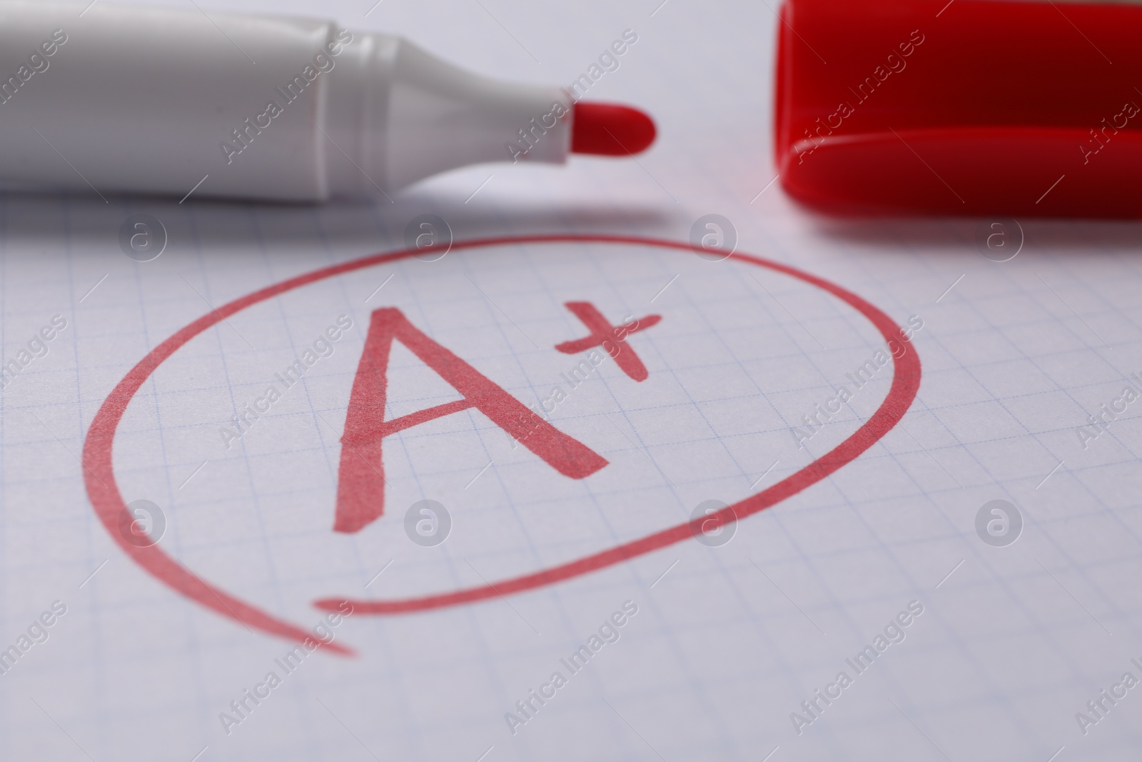 Photo of School grade. Red letter A with plus symbol on notebook paper and marker, closeup