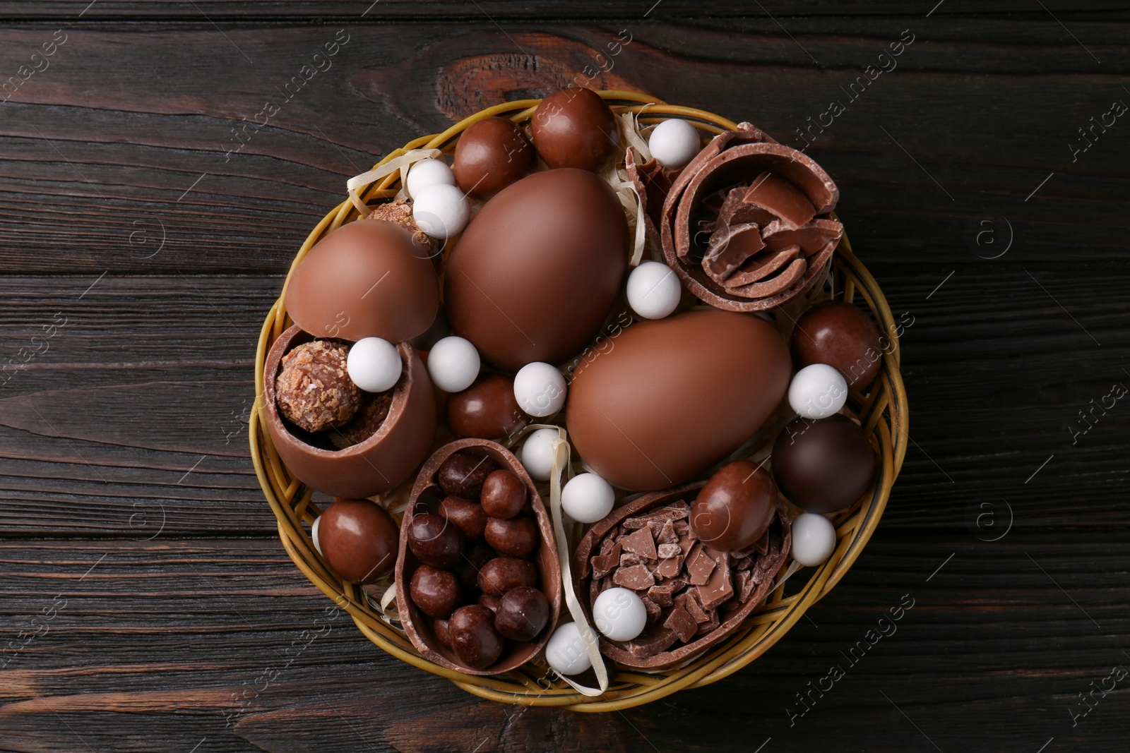 Photo of Tasty chocolate eggs and sweets in wicker basket on wooden table, top view