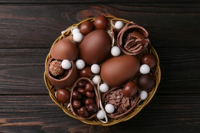 Photo of Tasty chocolate eggs and sweets in wicker basket on wooden table, top view