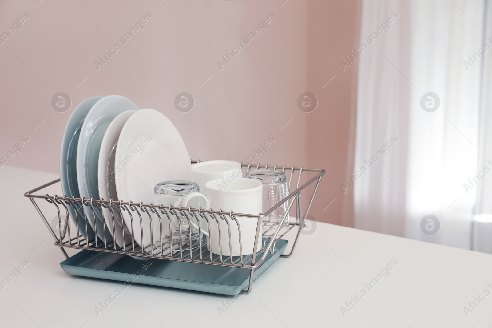 Photo of Dish drainer with clean dinnerware on table in kitchen. Space for text