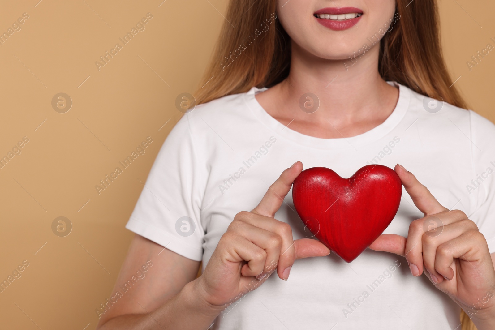 Photo of Young woman holding red heart on beige background, closeup with space for text. Volunteer concept