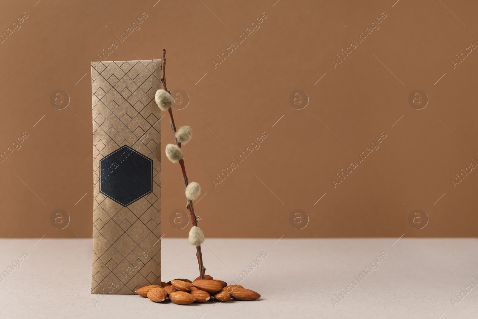 Photo of Scented sachet, pussy willow branch and almonds on grey table against brown background, space for text