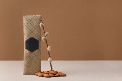 Photo of Scented sachet, pussy willow branch and almonds on grey table against brown background, space for text