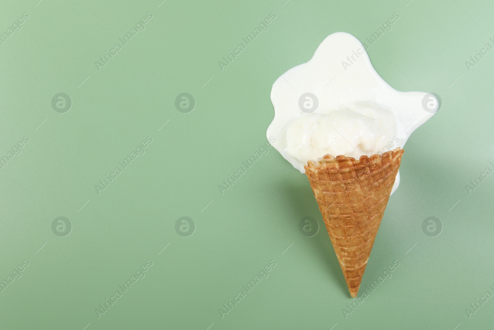 Photo of Melted ice cream and wafer cone on green background, top view. Space for text